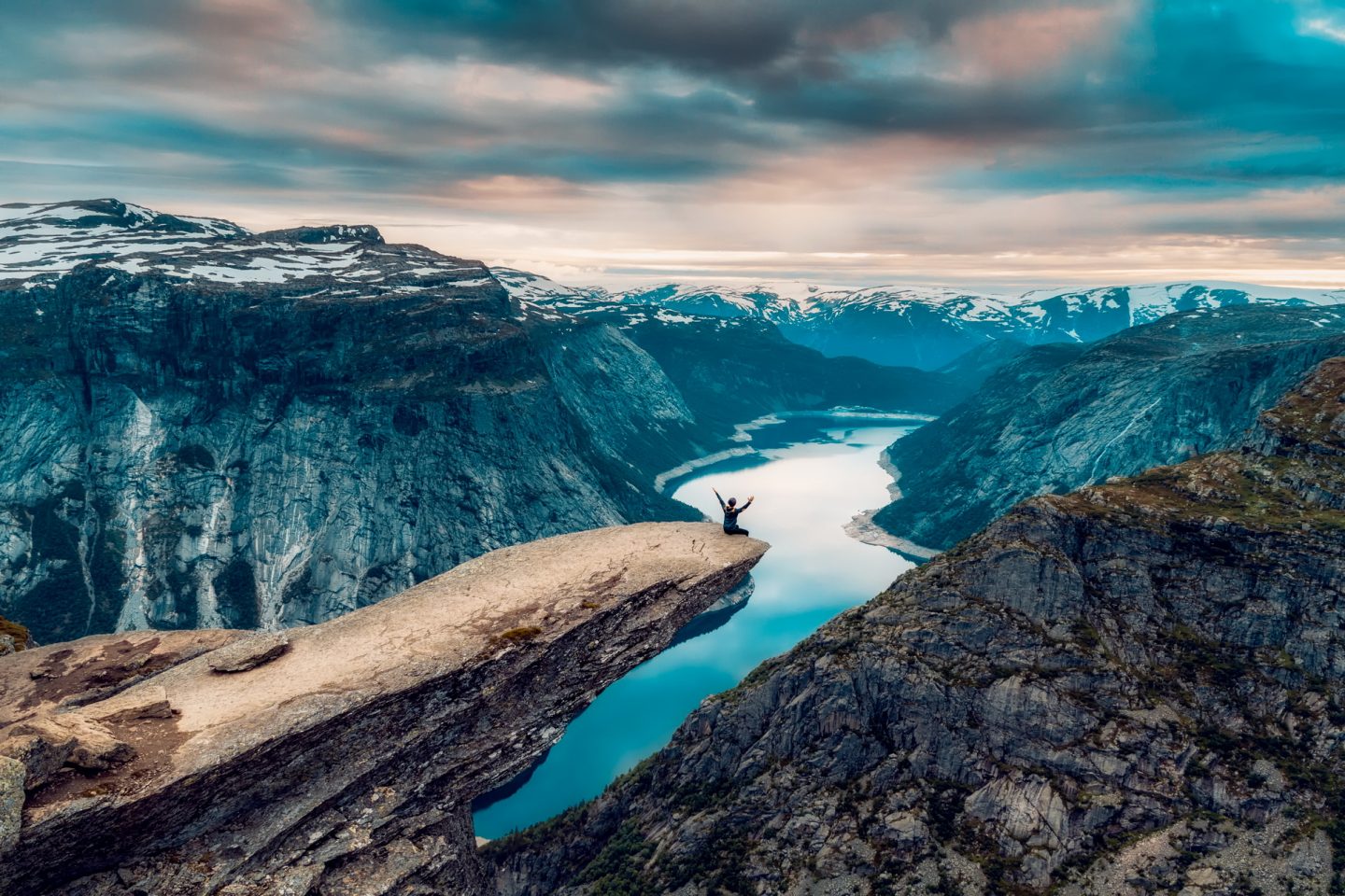A man sits on the cliff edge of Mount Trolltunga watching the sunset in the snowy Norwegian mountains near Odda, Rogaland, Norway